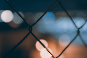Close-up of chain-link fence with blurred city lights at night