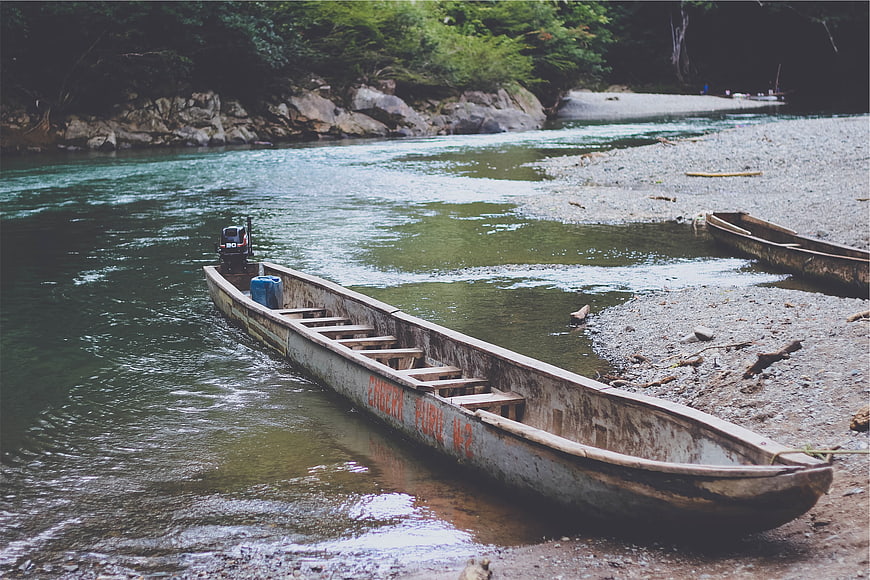 Weathered wooden boat on riverbank with forest background