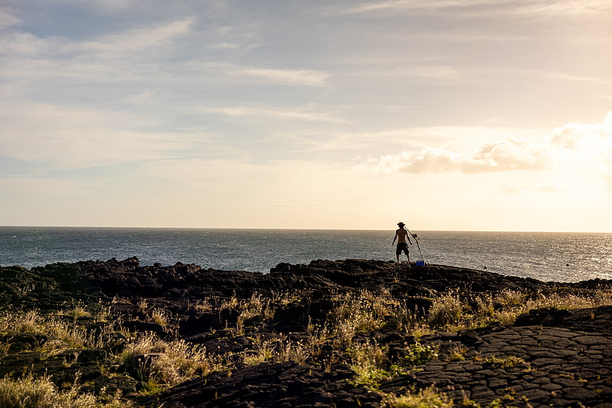 Silhouette of fisherman on rocky coast at sunrise