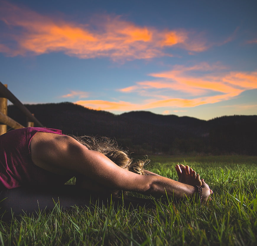 Woman stretching in grassy field at sunset