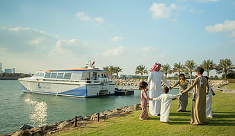 Middle Eastern family in traditional dress on waterfront lawn with catamaran
