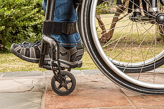 Close-up of wheelchair footrest and wheel on stone path