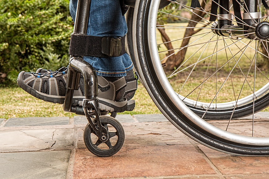 Close-up of wheelchair footrest and wheel on stone path