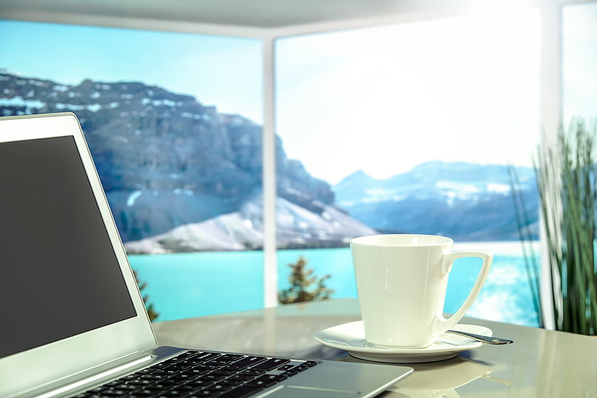 Laptop and coffee cup on desk with mountain lake view
