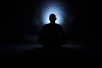 Silhouette of a person meditating in a dark room with a glowing blue aura