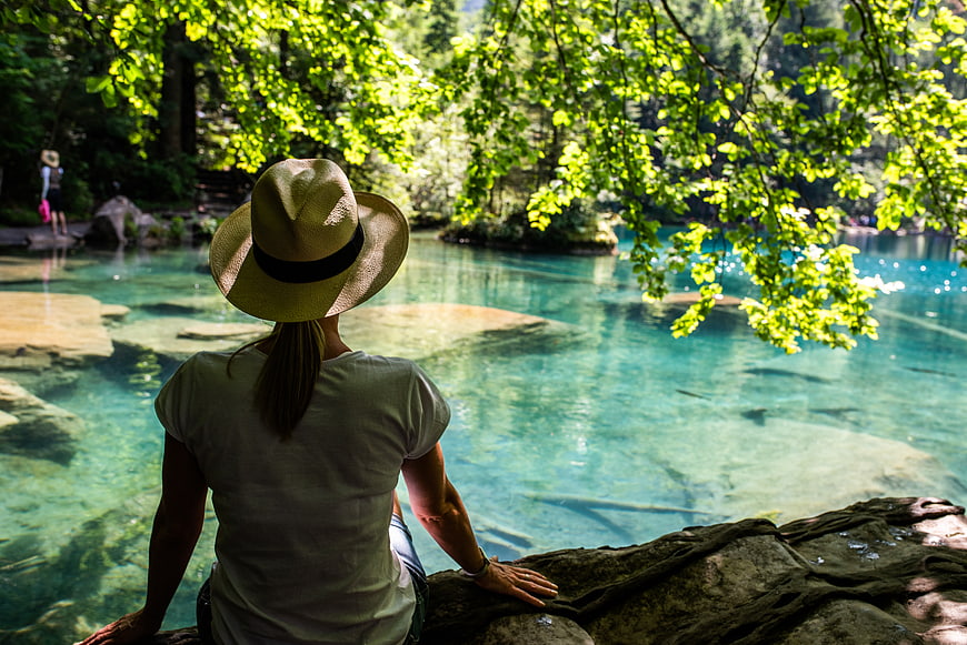 Woman in Hat Sitting by Turquoise River in Forest