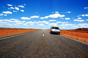 Silver car driving on outback road under blue sky