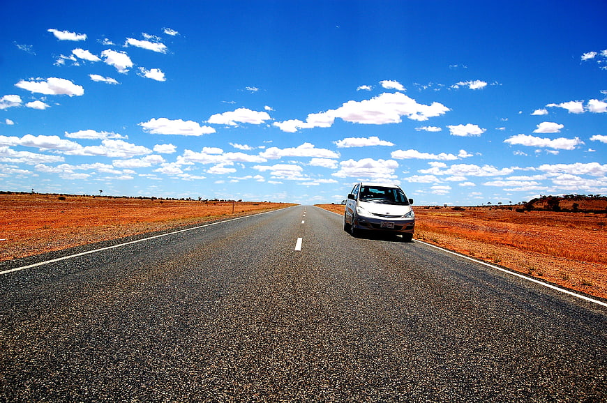 Silver car driving on outback road under blue sky