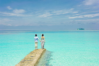 Couple holding hands on a concrete pier in turquoise tropical ocean