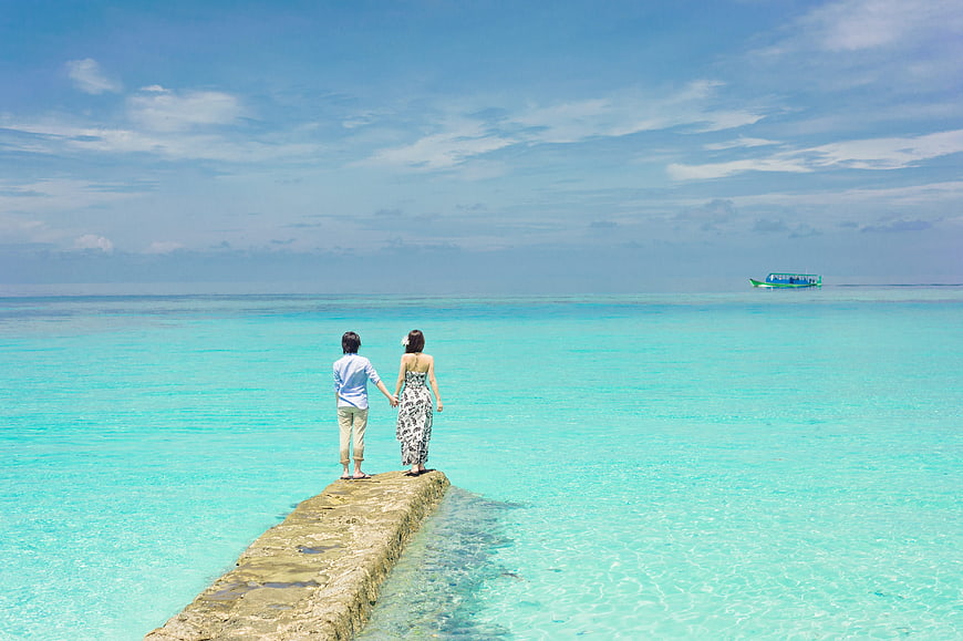 Couple holding hands on a concrete pier in turquoise tropical ocean