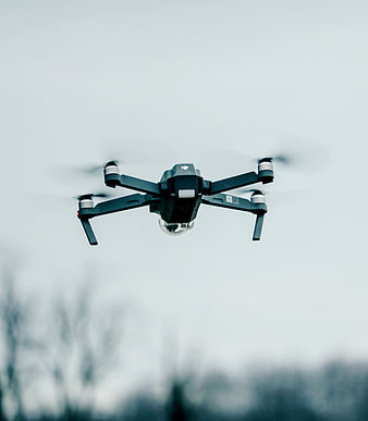 Black DJI drone flying against overcast sky