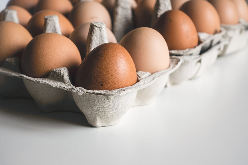 Close-up of brown eggs in a cardboard carton on white background