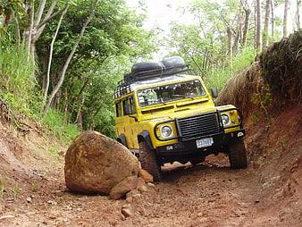 Yellow Land Rover Defender navigating rocky off-road trail in tropical forest