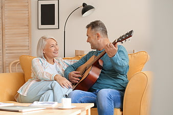 Happy senior couple playing guitar on yellow sofa at home