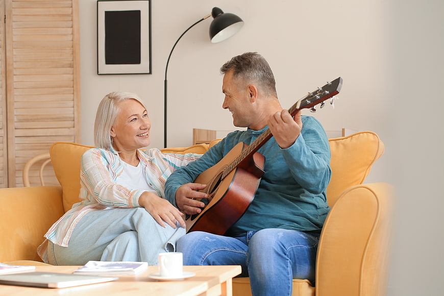 Happy senior couple playing guitar on yellow sofa at home