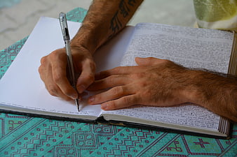Man Writing in Notebook on Patterned Tablecloth