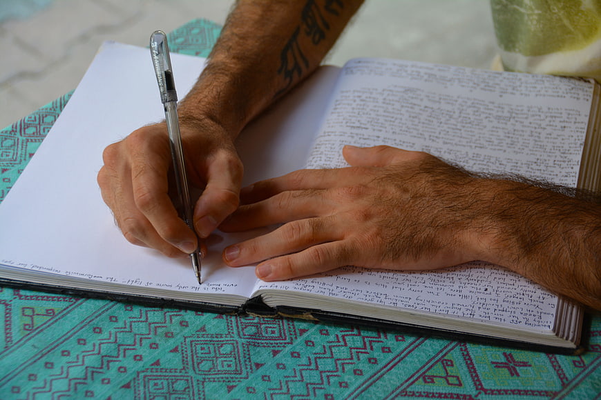 Man Writing in Notebook on Patterned Tablecloth
