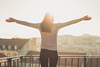 Woman with Outstretched Arms on Balcony at Sunset