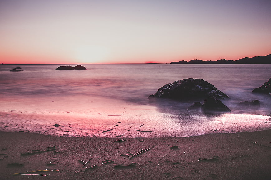 Serene Pink Sunset Beach with Silhouetted Rocks and Misty Ocean