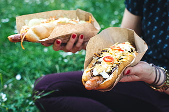 Hands holding loaded gourmet hot dogs outdoors