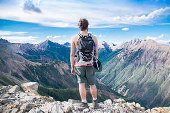 Hiker Standing on Rocky Mountain Summit Looking at Scenic View