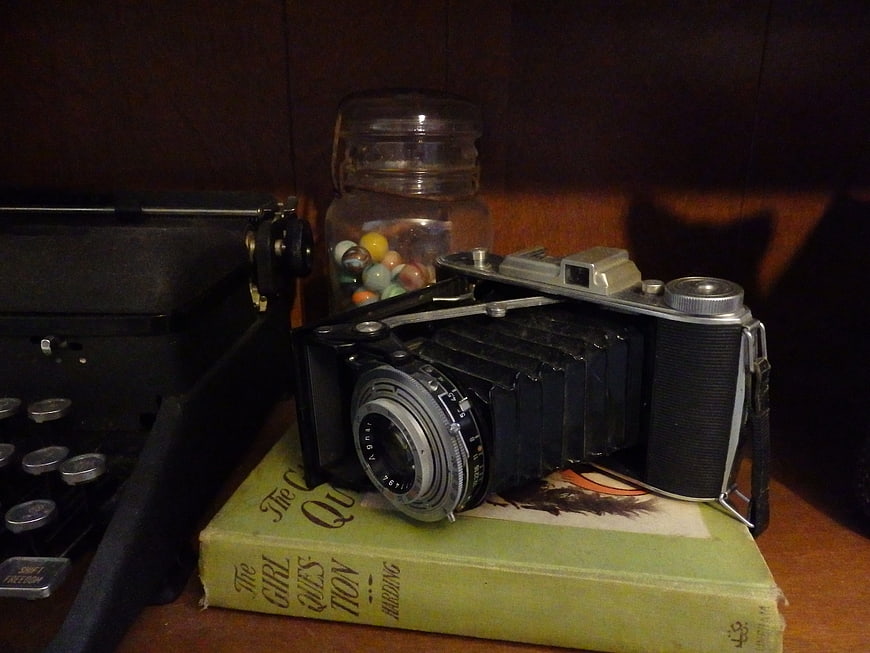 Vintage folding camera on book with typewriter and marbles