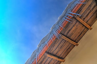 Icicles on wooden roof against blue winter sky