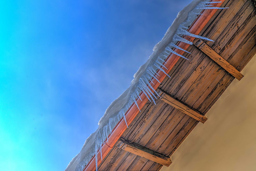 Icicles on wooden roof against blue winter sky
