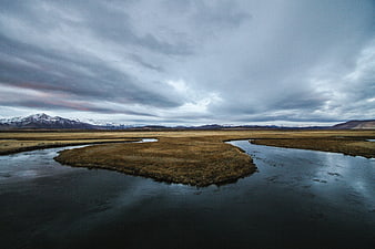 Dramatic landscape with winding river, grassy island, and snow-capped mountains