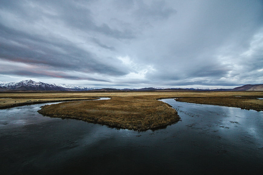Dramatic landscape with winding river, grassy island, and snow-capped mountains