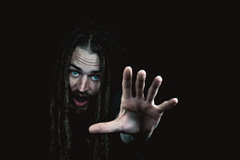 Man with dreadlocks reaching hand forward in dark moody portrait