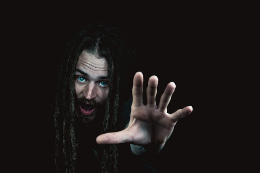 Man with dreadlocks reaching hand forward in dark moody portrait
