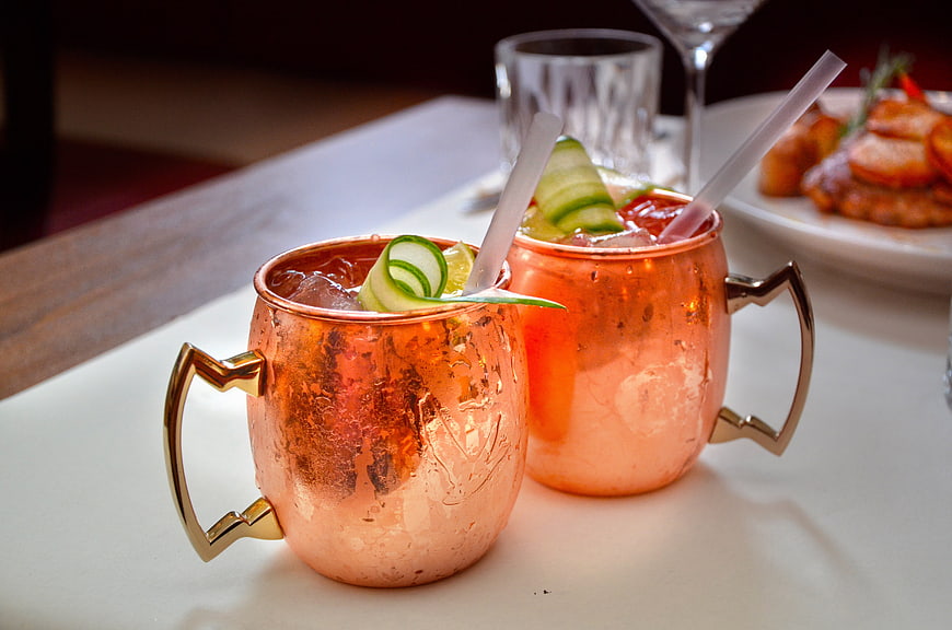 Two copper mugs with cucumber cocktails on a white table