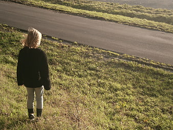 Young girl standing on grassy hill near road