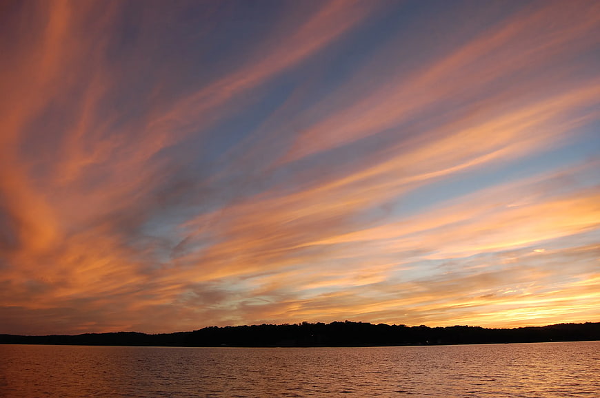 Vibrant orange and blue sunset clouds over calm lake silhouette