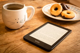 Cozy e-reader, cat mug, and donuts on rustic wooden table