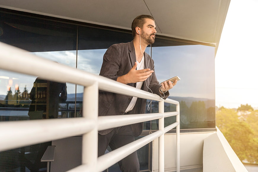 Businessman talking on phone with headphones on balcony