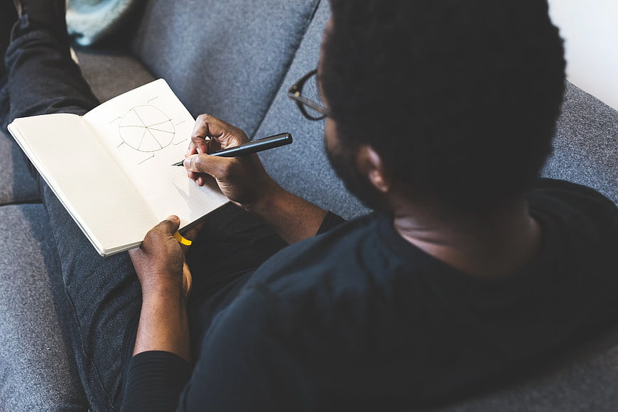 Man sketching diagram in notebook on gray couch