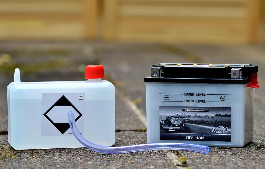 Motorcycle battery and acid refill container on pavement