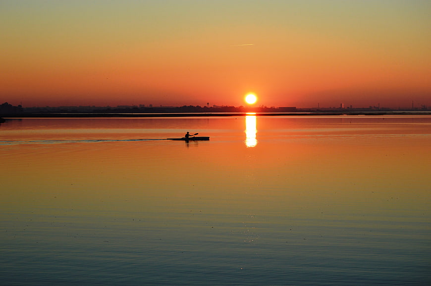 Silhouette of a Canoeist Paddling on a Calm Lake at Sunset