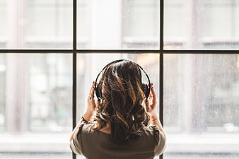 Woman with headphones listening to music by rainy window
