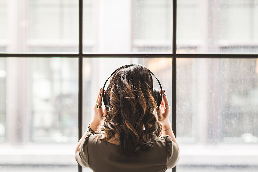 Woman with headphones listening to music by rainy window