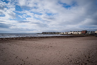 Coastal town view from sandy beach under cloudy sky