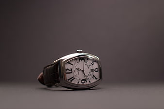 Luxury silver wristwatch with brown leather strap on gray background