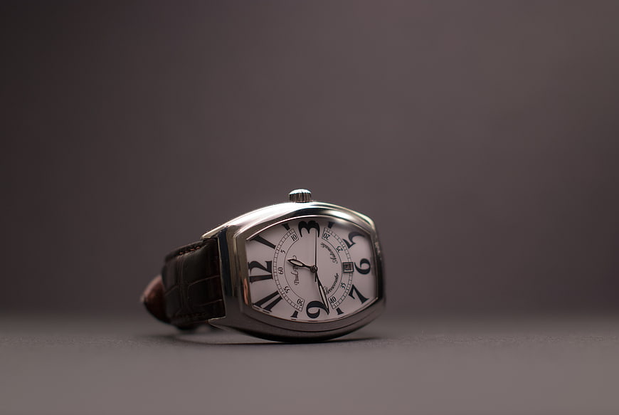 Luxury silver wristwatch with brown leather strap on gray background