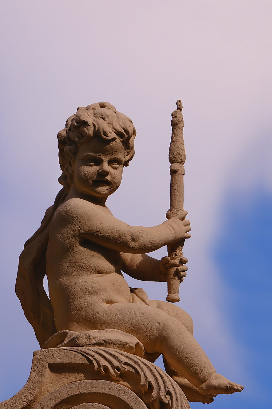 Stone cherub statue holding a torch against blue sky