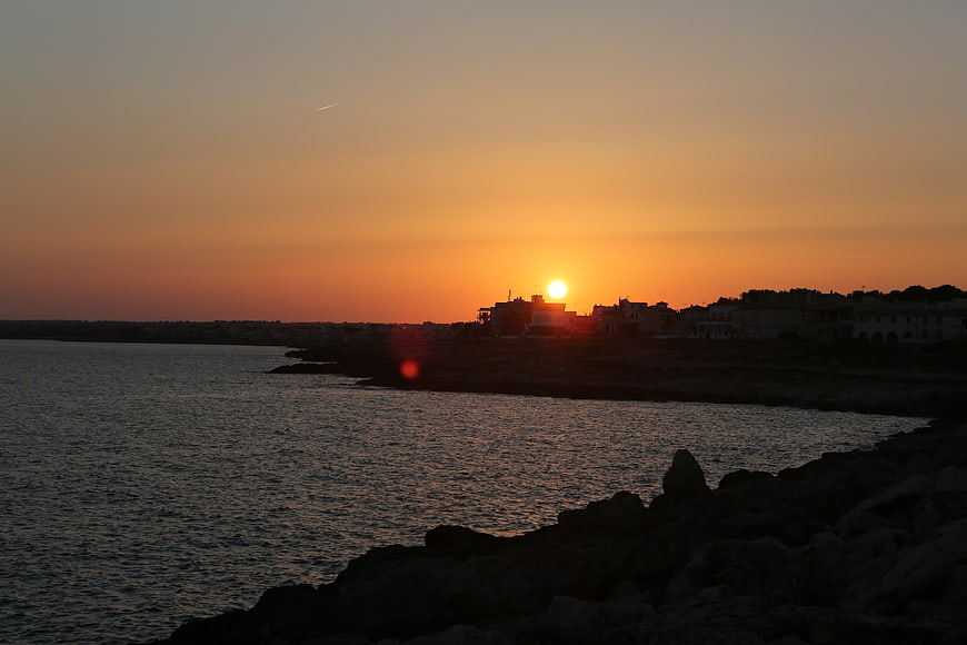 Sunset over coastal town with silhouetted buildings and rocky shore