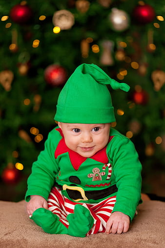 Baby in Green Elf Costume Sitting in Front of Christmas Tree