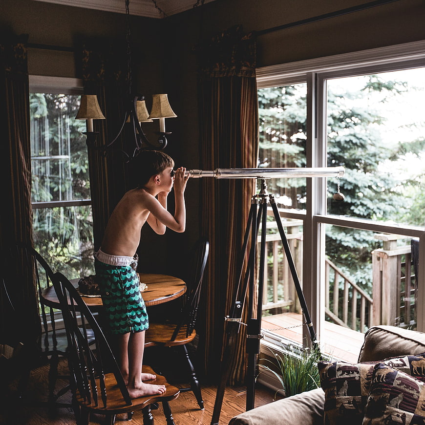 Young boy looking through telescope in sunlit living room