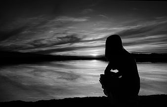 Silhouette of woman sitting by lake at sunset black and white
